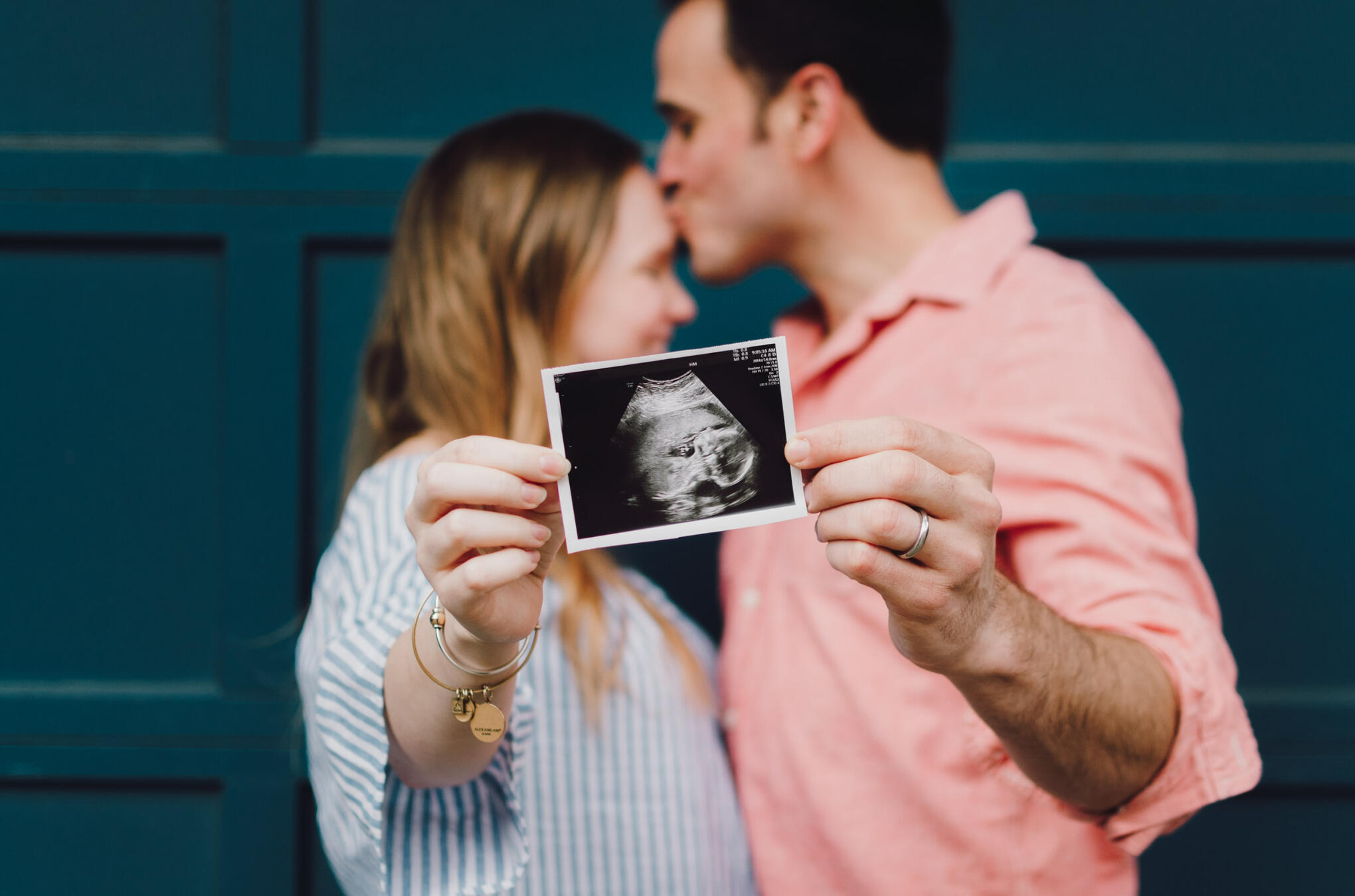 A couple embraces as they hold an ultrasound photo
